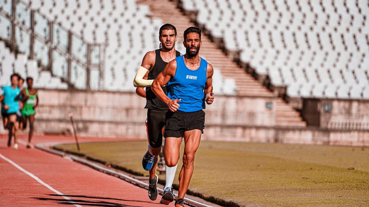 Focused male runners competing on a sports track during a daytime race in a stadium setting.